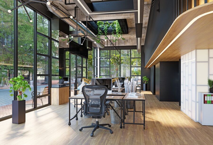 Modern office workspace with desks, chairs, large windows, and indoor plants in a bright building lobby